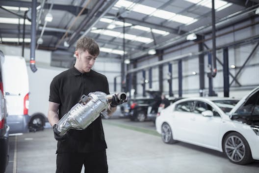 Apprentice holding catalytic converter in shop