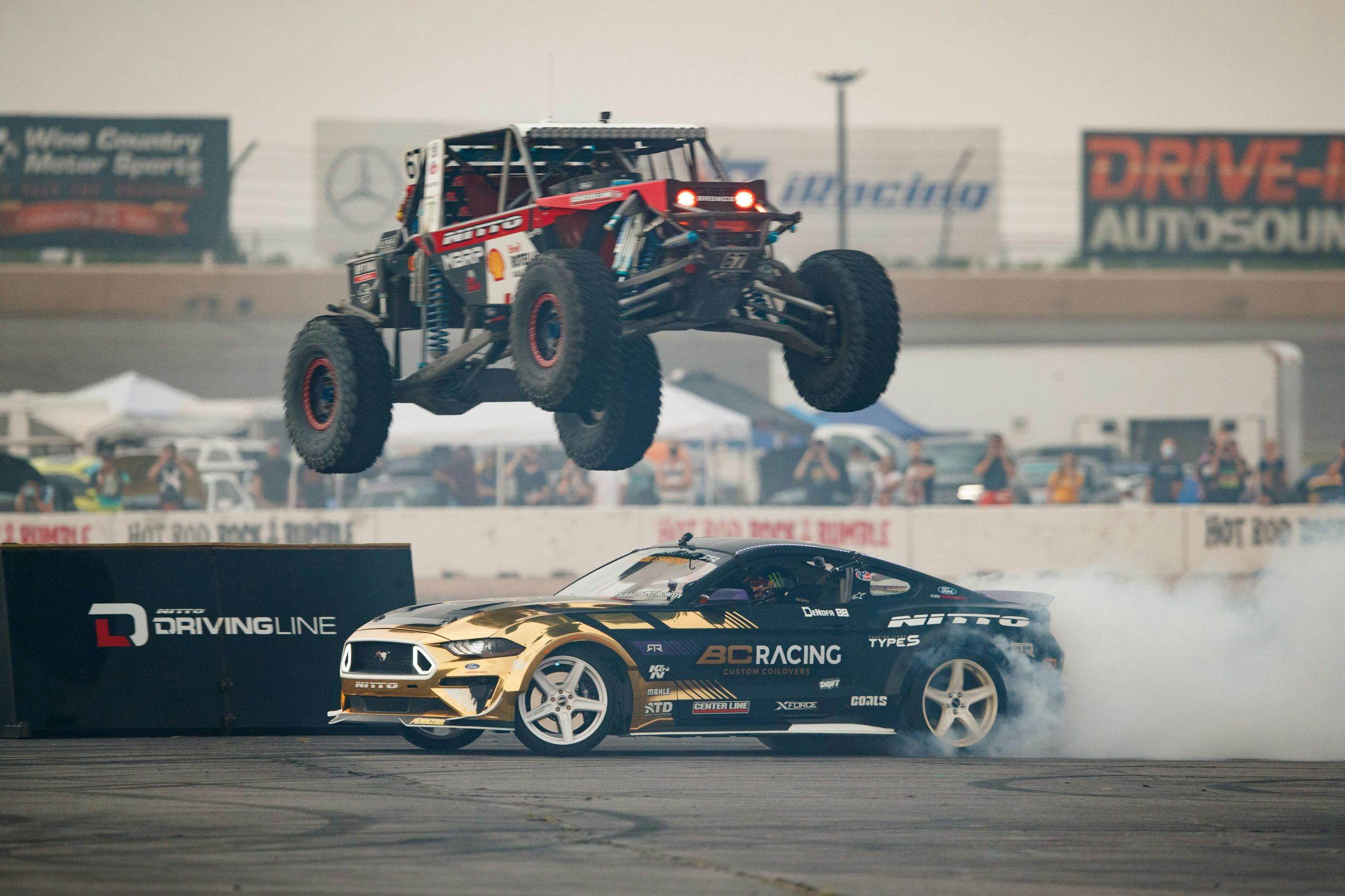 Off-road vehicle jumps over golden Mustang at GridLife event