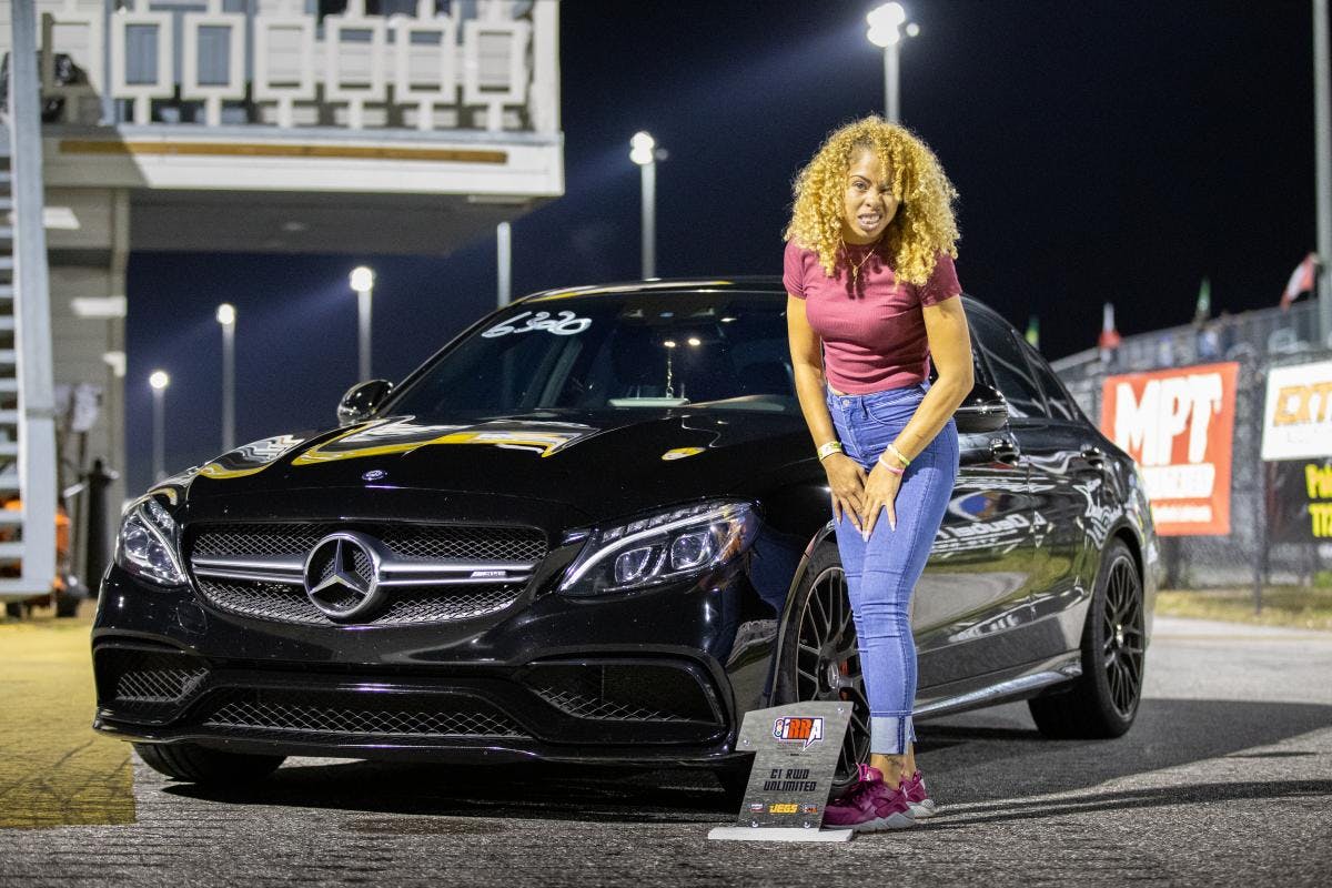 Roll race winner stands by her Mercedes-Benz sedan with her trophy