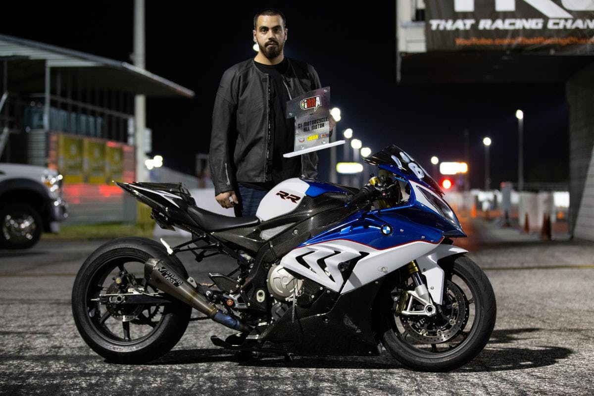 Roll race winner stands behind his motorcycle while holding trophy