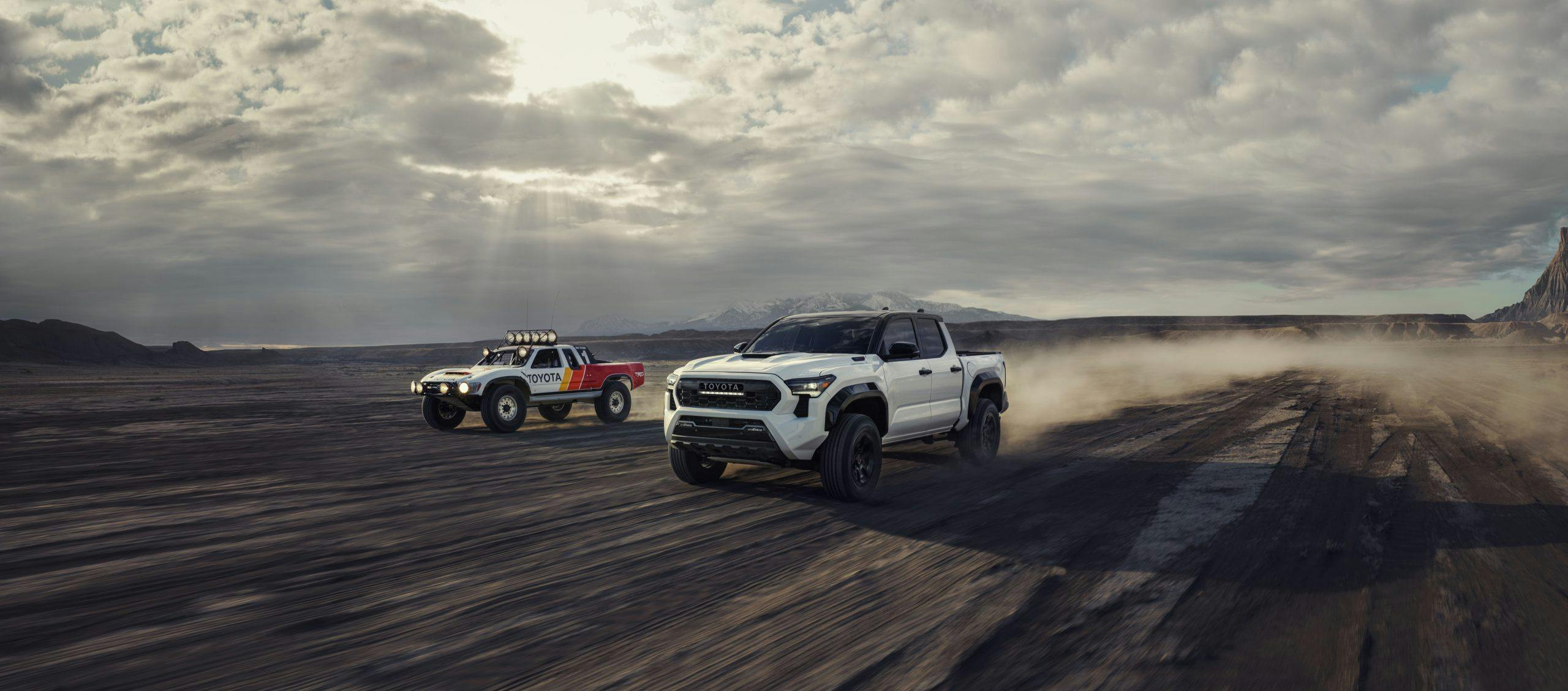 2024 Toyota Tacoma TRD Pro and Trophy Truck exterior front three quarters storming across the desert