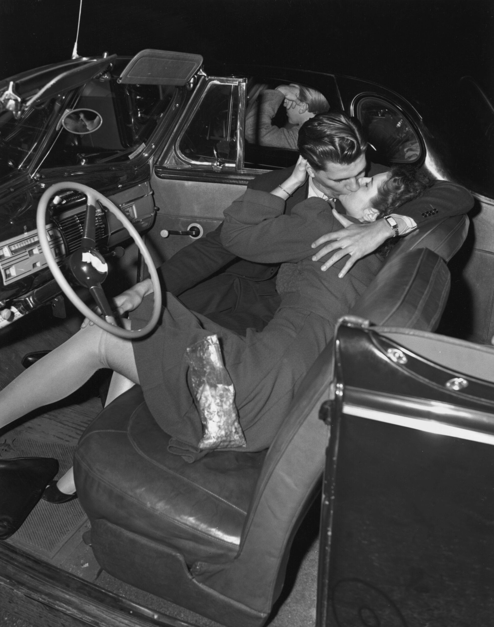 couple kissing in the front seat of a convertible car at a drive-in movie theater