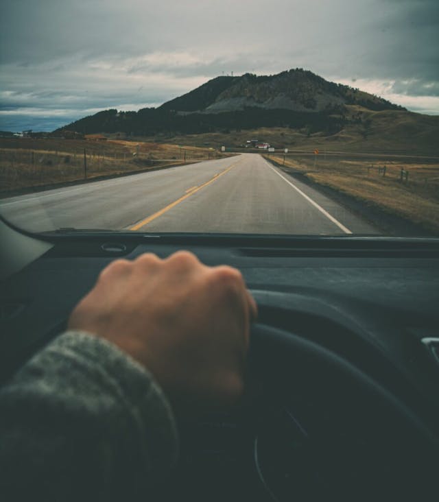 open road hilltop horizon hand on wheel linear perspective