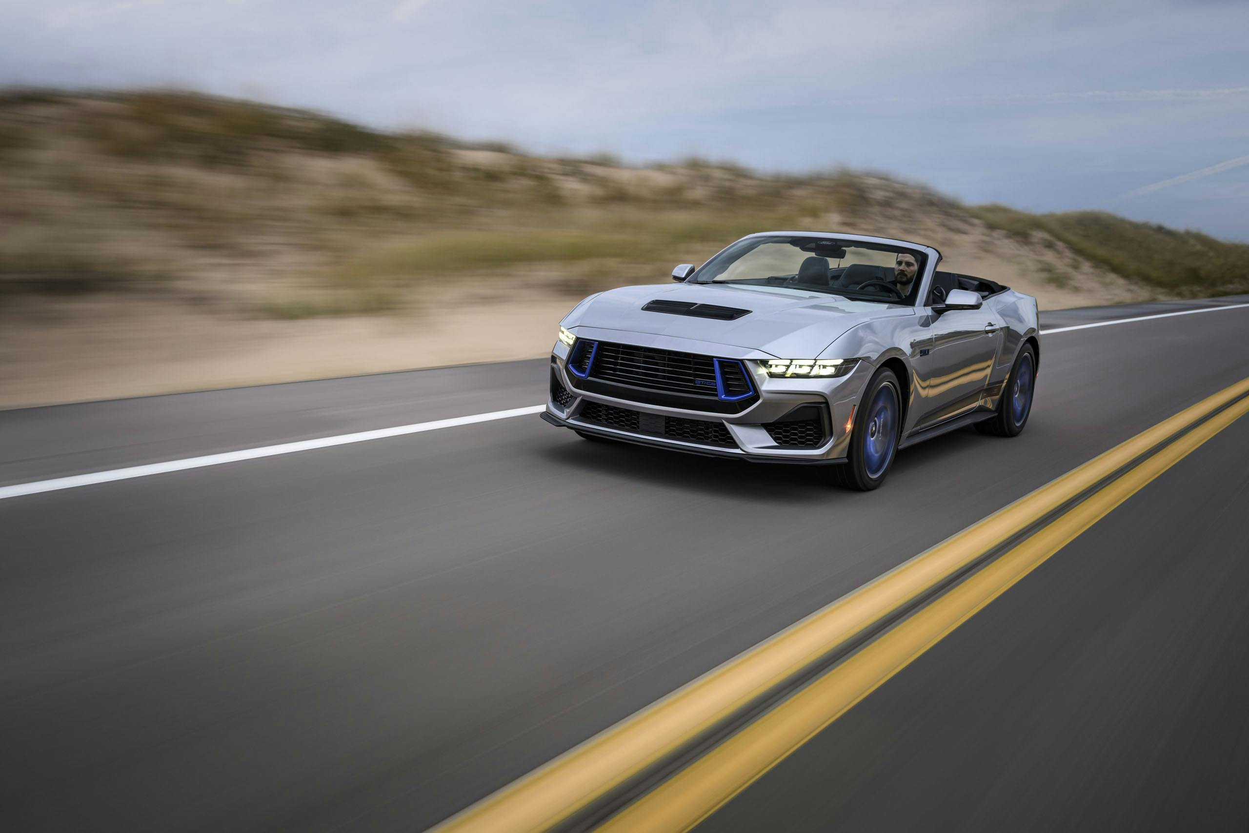 2024 Ford Mustang GT California Special exterior front three quarter convertible driving by dune