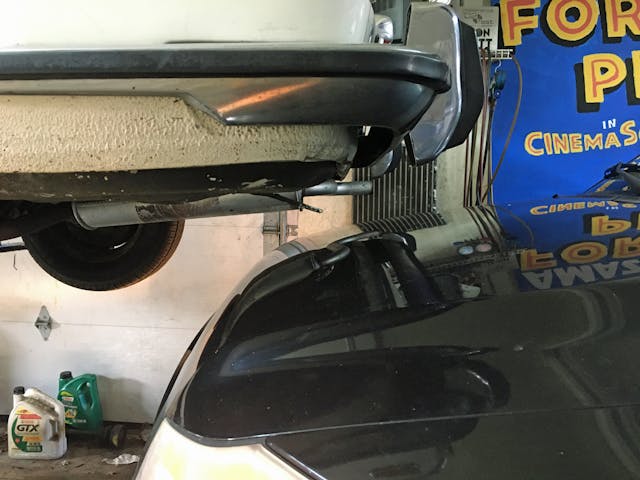 DIY exhaust repair car tail end underside on lift over hood of another car