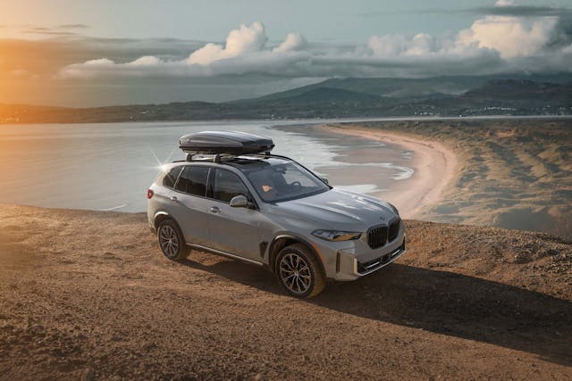 2025 BMW X5 Silver Anniversary Edition exterior high front three quarter with roof box at beach