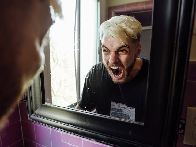 Frustrated young man screaming into mirror