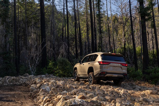 2025 Lexus LX 700h Overtrail off-roading exterior rear three quarter going over rock garden